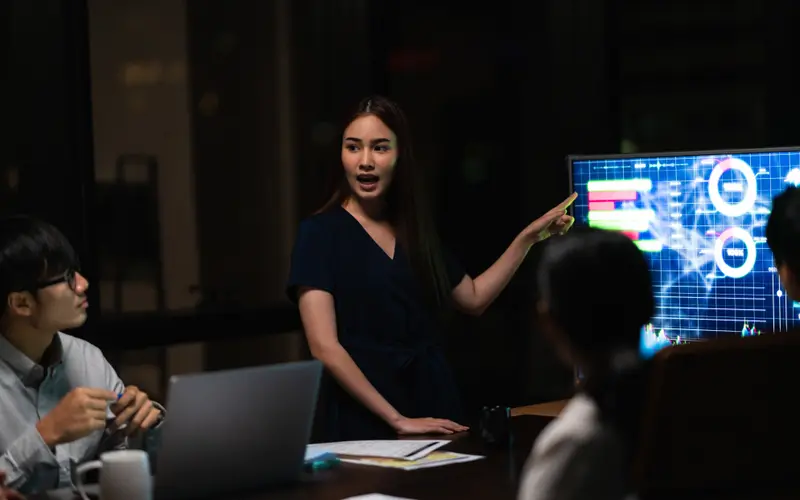 A small team working late in a dark office, presenting charts on a screen