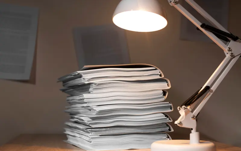 A tall stack of paper documents waiting on a desk